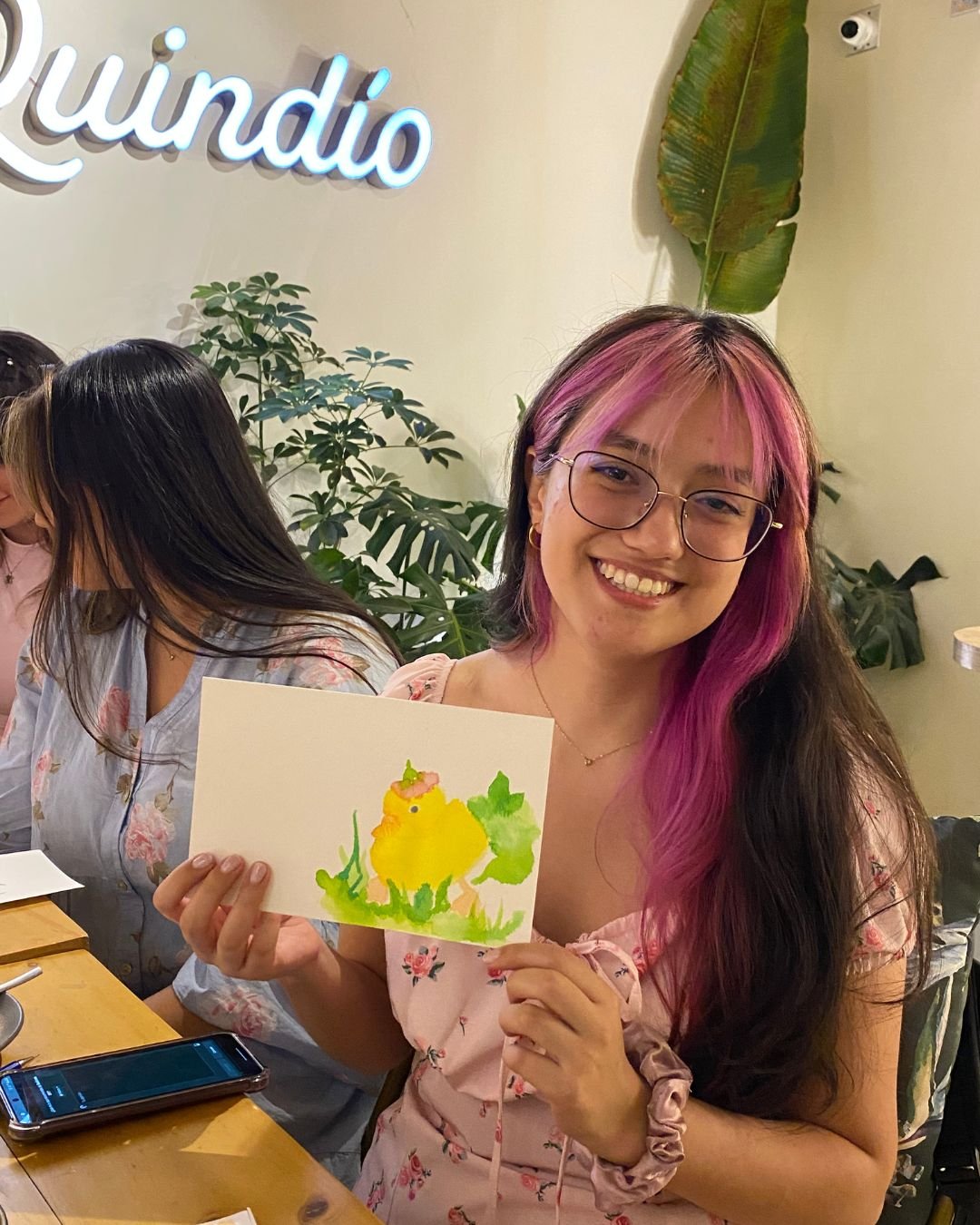 Participante sonriendo con su acuarela de un pollito amarillo, hecha en uno de nuestros talleres de arte