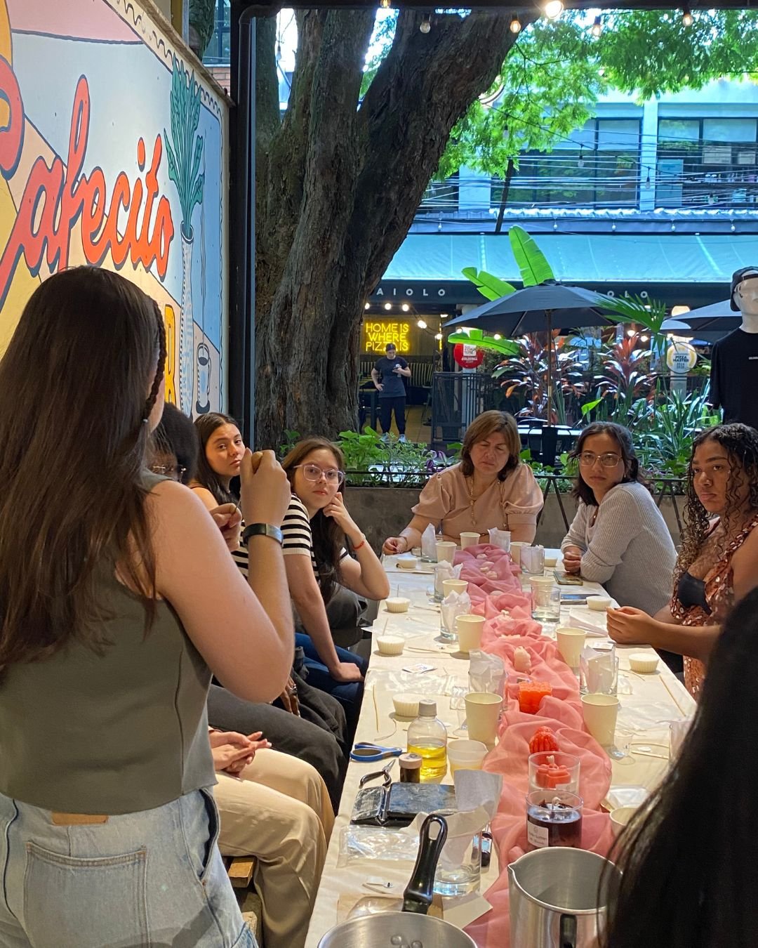 Grupo reunido en una mesa larga al aire libre con materiales para hacer velas, durante uno de nuestros talleres de arte