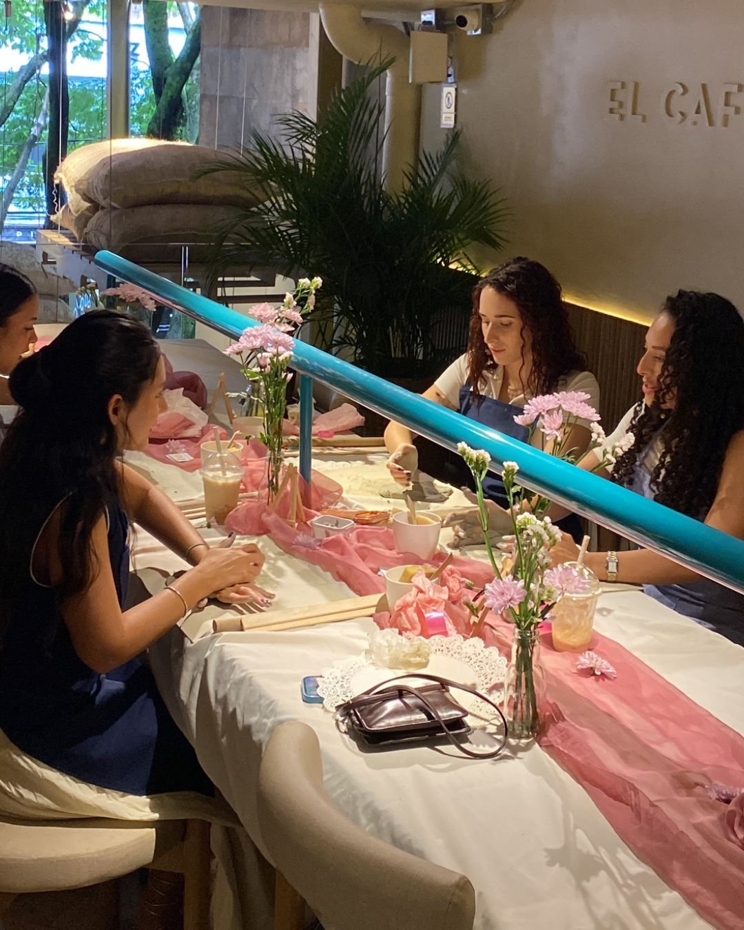 Mujeres creando con sus manos en una mesa con flores y tela rosa, durante nuestros talleres de arte