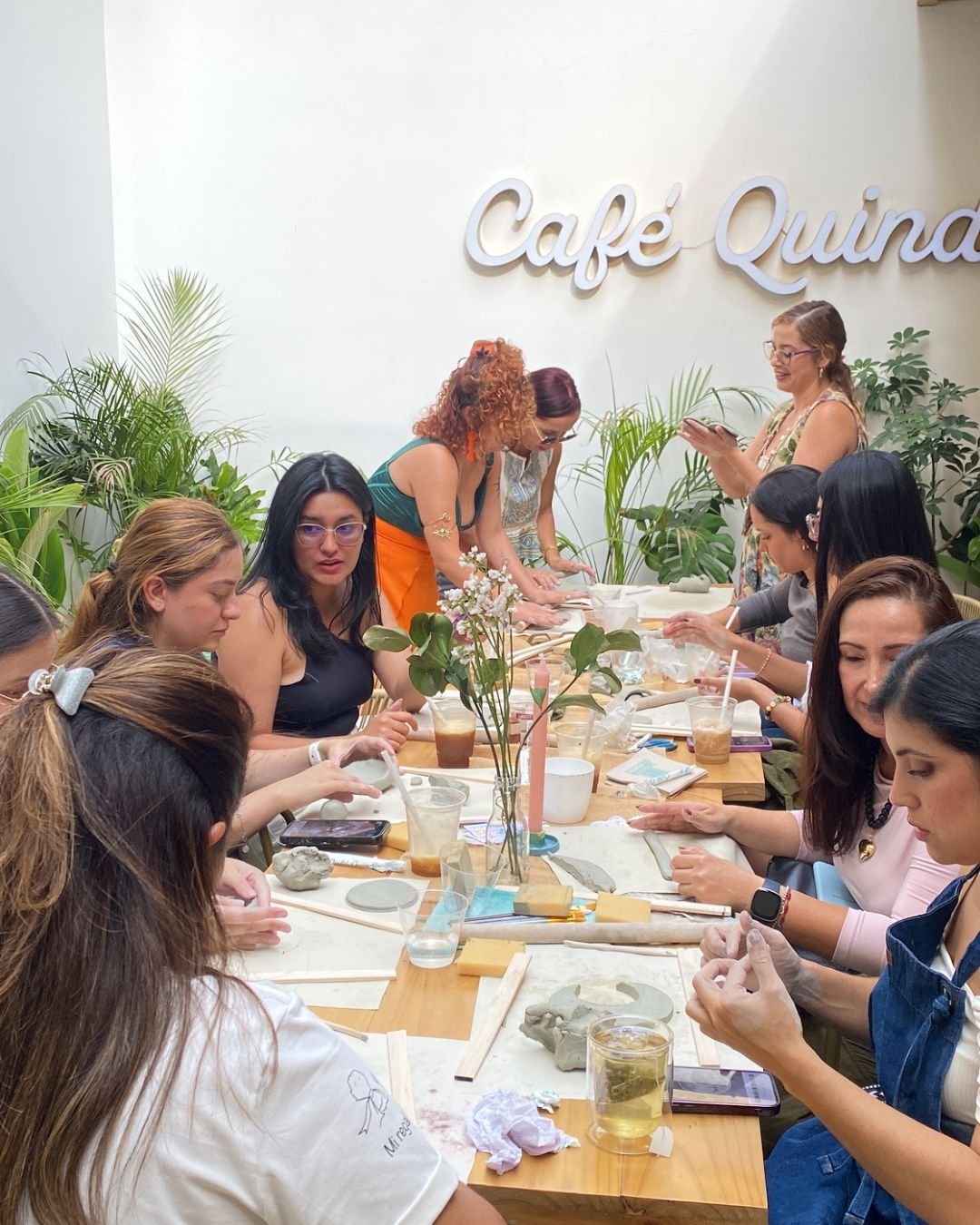 Grupo de mujeres moldeando arcilla en una mesa larga rodeada de plantas, en nuestros talleres de arte en Medellín