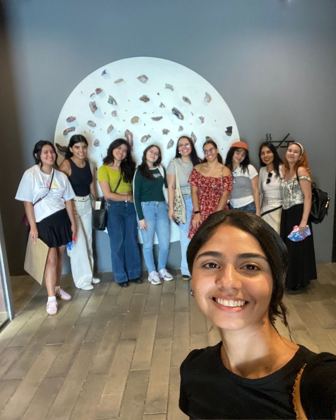 Selfie grupal de mujeres sonriendo frente a una escultura circular blanca, tras una salida de nuestros talleres de arte