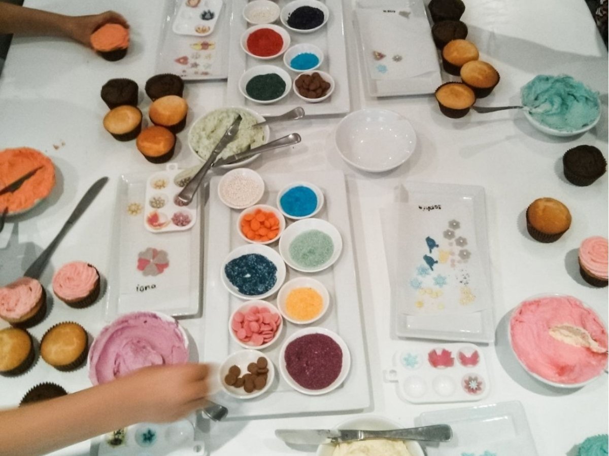Mesa con cupcakes, glaseados de colores y cuencos de toppings en el Cupcake Bar, uno de nuestros talleres de arte